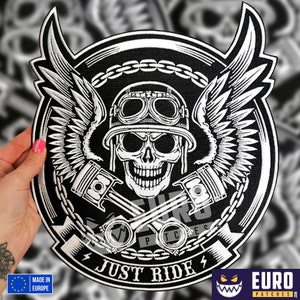 Pode incluir: Patch bordado em preto e branco com uma caveira usando capacete e óculos, pistões cruzados e asas. O patch tem uma borda de corrente e o texto "Just Ride".