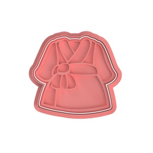 Op de afbeelding: Een roze badjas koekjesvormer met een witte omtrek. De badjas heeft een riem die in de taille is geknoopt.