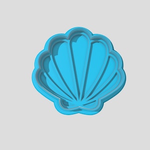 May include: A light blue plastic seashell cookie cutter. The cutter is shaped like a seashell with a detailed design.