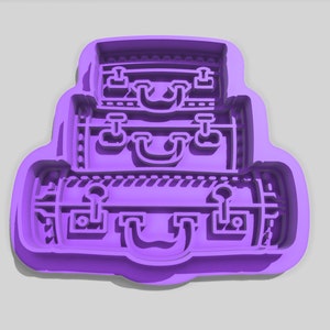 Può includere: Tagliapasta in plastica viola a forma di pila di tre valigie. Le valigie hanno un design dettagliato con maniglie e fibbie.