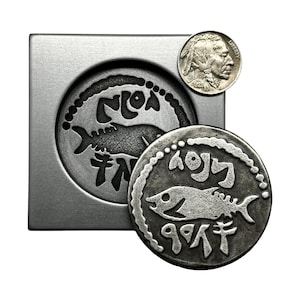 May include: A silver coin with a fish design and Hebrew lettering. The coin is next to a mold of the coin, and a US Buffalo nickel is in the background.