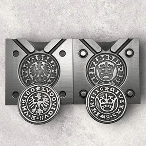 May include: Two metal molds for making coins. The molds are silver in color and have a circular indentation in the center. The molds are labeled with the text "DIVI", "IVDO", "B.M.V", "8.8", and "DIVI", "G.R", "B.M.V", "8.8".