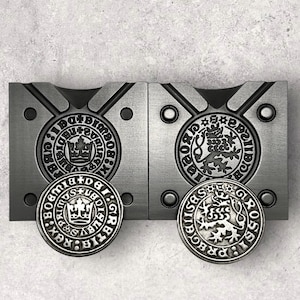 May include: Two silver coins with a raised design. The coins are in a mold for making replicas. The coin on the left has the text "BIBLIOTHECA + BOHEMIA" and a crown. The coin on the right has the text "SIG. ROS. + BOHEMIA" and a lion.