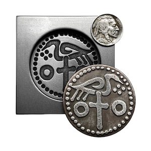 May include: A silver metal mold with a design of a bird and cross inside a circle. A silver coin with the same design is next to the mold. A silver coin with a profile of a Native American man is in the top right corner.