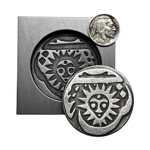 May include: A silver metal mold with a circular design of a sun with a face inside. A silver metal coin with the same design is sitting next to the mold. A silver coin with a profile of a Native American man is in the upper right corner of the image.