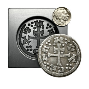 May include: A silver coin with a cross design and a circular border. The coin is sitting on a metal surface with a similar design.