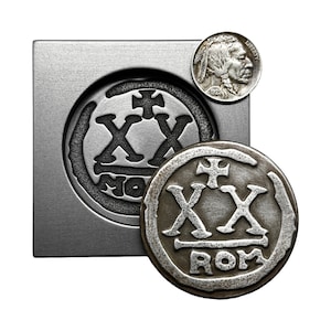 May include: A silver metal mold with a round impression of a coin with the text "XX" and "ROM". A silver coin with the text "XX" and "ROM" is sitting next to the mold. A silver coin with a profile of a Native American person is sitting on top of the mold.