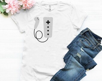 May include: White t-shirt featuring a grey graphic of a video game controller and a remote.