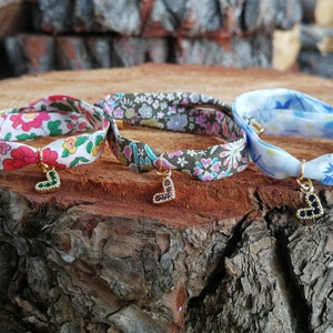 May include: Three fabric bracelets with heart-shaped charms. The bracelets are made of different patterned fabrics: pink and white floral, green and white floral, and blue and white floral. The charms are gold with different colored gemstones.