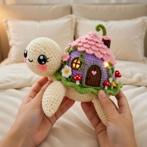May include: A crocheted turtle with a house on its back. The house has a pink roof, purple walls, and a brown door. The turtle is cream-colored with a smiling face and rosy cheeks. The house is decorated with flowers and mushrooms.