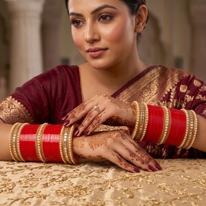 Op de afbeelding: Een set felrode armbanden met goudkleurige accenten en kleine witte parelachtige kraaltjes. De armbanden worden gedragen om beide polsen, die versierd zijn met ingewikkelde hennapatronen, en een gouden ring is zichtbaar op een vinger.