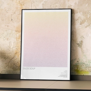 May include: A framed vertical poster featuring a soft gradient transitioning from pale yellow at the top to light purple at the bottom. The text DUCK SOUP is printed in the lower left corner, with additional small text details in the lower right corner.