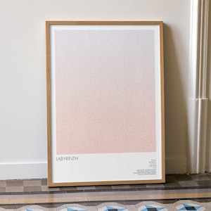 Puede incluir: Una impresión artística enmarcada titulada "LABYRINTH" con un diseño degradado en tonos rosa, blanco y gris. La obra de arte está en un marco de madera y se apoya en una pared blanca. La impresión se exhibe en un suelo de baldosas estampadas.