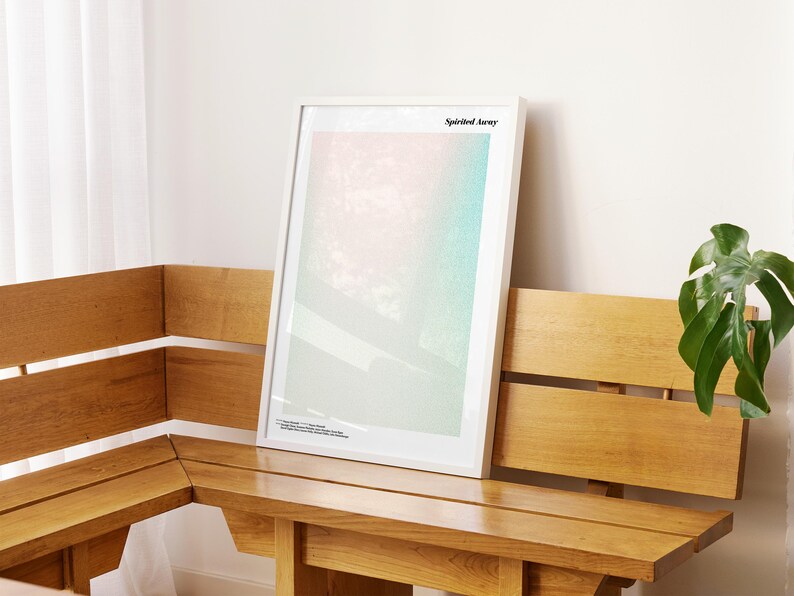 a wooden bench with a framed artwork hanging on it, placed in a room with a window and a plant.