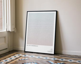 May include: A framed art print titled "ON THE WATERFRONT" leans against a wall. The artwork features a gradient of colors, transitioning from blue to gray to pink. The frame is black, and the print is displayed on a patterned tile floor.