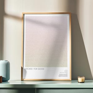 Op de afbeelding: Een ingelijste kunstdruk met een gradiëntontwerp in zachte roze, beige en groene tinten. De print wordt weergegeven op een mintgroen oppervlak, naast een blauwe vaas, een houten doos en een brandende kaars. De tekst "WICKED: FOR GOOD" is zichtbaar.
