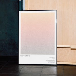 Op de afbeelding: Een ingelijste poster met een gradiëntachtergrond van perzik-, roze- en grijstinten. De poster heeft de tekst "PULP FICTION" onderaan, met extra tekst eronder. De lijst is zwart en de poster leunt tegen een muur.