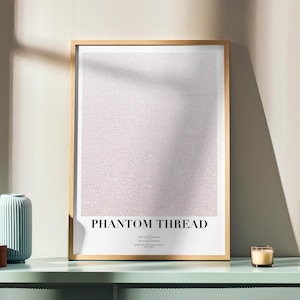 Può includere: Una stampa artistica incorniciata con il testo "PHANTOM THREAD" in stile minimalista. La stampa ha uno sfondo strutturato rosa chiaro e bianco. Un vaso azzurro, una scatola di legno e una candela sono su una superficie verde menta.