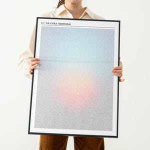 May include: A framed poster featuring the text "E.T. The Extra-Terrestrial" at the top. The artwork has a gradient background of blue, pink, and yellow, with small text filling the space. The frame is black.