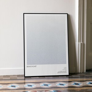 May include: A framed art print with a black border, leaning against a white wall. The print features a gradient of gray tones and the word "BRAVEHEART" at the bottom. The print is displayed on a patterned tile floor.