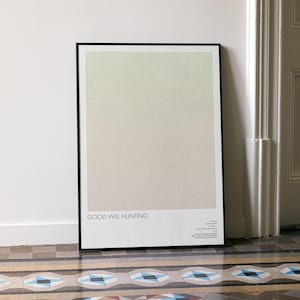 May include: A framed poster with a black border, leaning against a white wall. The poster features a gradient of colours, transitioning from light green to beige. The text "GOOD WILL HUNTING" is at the bottom.