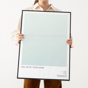 Może przedstawiać: Oprawiony plakat z czarną ramką, z jasnoniebieskim i białym gradientowym tłem. Tekst "CALL ME BY YOUR NAME" znajduje się na dole, z dodatkowym tekstem poniżej. Plakat jest trzymany na białym tle.