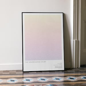 May include: A framed art print featuring a gradient of colors, transitioning from yellow to pink. The black frame leans against a white wall. The text "THE NEVERENDING STORY" is visible at the bottom of the print.