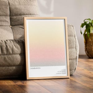 Pu&ograve; includere: Una stampa artistica incorniciata con un design sfumato nei toni del giallo, rosa e grigio. La stampa &egrave; intitolata "Casablanca" ed &egrave; esposta in una cornice di legno chiaro. L'opera d'arte &egrave; appoggiata a un divano grigio imbottito, con una pianta in un cesto di vimini.