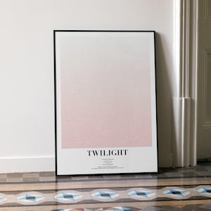 May include: A framed art print with a gradient design, transitioning from white to a soft pink hue. The word "TWILIGHT" is printed in black at the bottom. The artwork is leaning against a white wall.