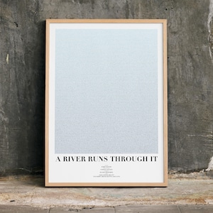 Può includere: Una stampa artistica incorniciata con un design a gradiente blu chiaro. La stampa è in una cornice di legno chiaro e presenta il testo "A RIVER RUNS THROUGH IT" in basso. L'opera d'arte è esposta contro un muro grigio strutturato.