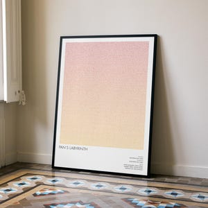 May include: Framed art print featuring a gradient of pink and yellow hues. The artwork, titled "Pan's Labyrinth," is displayed in a black frame and leans against a white wall. The print includes text at the bottom.