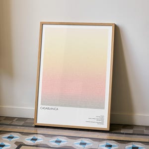 Pu&ograve; includere: Una stampa artistica incorniciata con un design a gradiente nei toni del giallo, rosa e grigio. La parola "CASABLANCA" &egrave; stampata in basso, insieme a testo aggiuntivo. L'opera d'arte &egrave; esposta contro un muro bianco e poggia su un pavimento piastrellato.