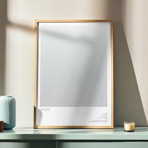 Op de afbeelding: Een ingelijste kunstdruk met het woord "GHOST" onderaan. De print heeft een lichtgrijze gradiënt achtergrond. Een lichtblauwe vaas, een houten doos en een brandende kaars staan op een mintgroen oppervlak.