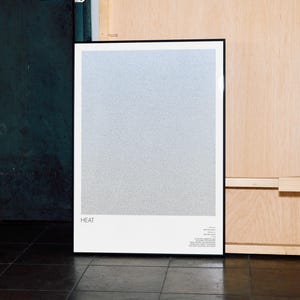 May include: A framed art print with a gradient design, transitioning from light blue to gray. The word "HEAT" is printed in white at the bottom left. Additional text is present in the lower right corner. The frame is black.