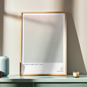 May include: A framed poster with the text "WHEN HARRY MET SALLY" at the bottom. The poster has a light wood frame and a textured, gradient background. A blue vase, a wooden box, and a candle sit on a mint green surface.