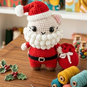 Può includere: Una figura di Babbo Natale fatta a mano all'uncinetto, con abito e cappello rossi, barba bianca. Una piccola borsa rossa con un fiocco bianco è accanto alla figura. Sul piano di legno ci sono anche rocchetti di filo colorato, forbici e agrifoglio decorativo.