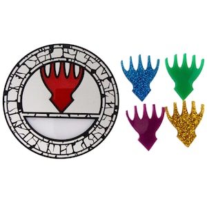 May include: A circular black and white emblem with a red design, and four glittery claw-shaped embellishments in blue, green, purple, and gold. The emblem has a white interior with a red arrow-like shape.