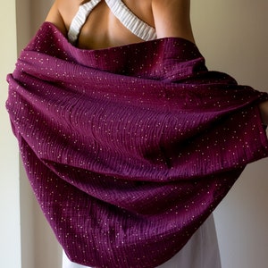 May include: A burgundy shawl with gold glitter dots. The shawl is draped over a person's shoulders.