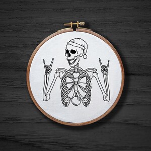 May include: Embroidered hoop art featuring a skeleton wearing a Santa hat and giving the peace sign with both hands.