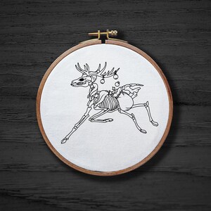 May include: A white embroidery hoop with a black line drawing of a skeletal reindeer with ornaments on its antlers. The reindeer is running to the right.