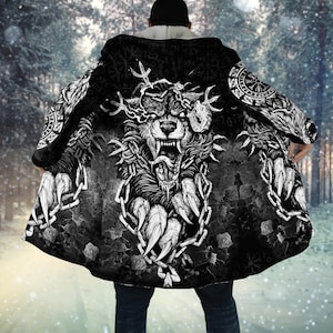 May include: A black and white hooded cloak featuring a large graphic of a snarling wolf head surrounded by heavy chains and Norse-inspired circular symbols. The garment has a white fleece-lined interior and a long, open-front design.