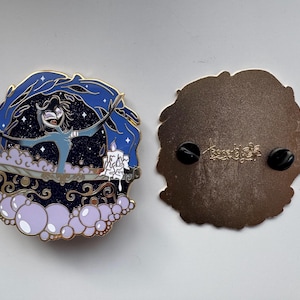 May include: A circular enamel pin featuring a character in a bathtub with purple bubbles, a lit candle, and a dark blue starry background. The reverse side is metallic brown with two black rubber pin backs and an engraved signature logo.