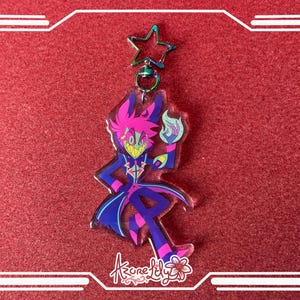 May include: A colorful acrylic keychain featuring a cartoon character with a magenta and blue color scheme. The character is holding a blue flame. The keychain has a star-shaped clasp and the text "Azure Lily".