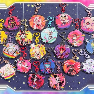 May include: A selection of character keyrings with heart-shaped clasps. The keyrings showcase various cartoon characters in bright colours, set against a dark blue background with stars. The keyrings are round and have a glossy finish.