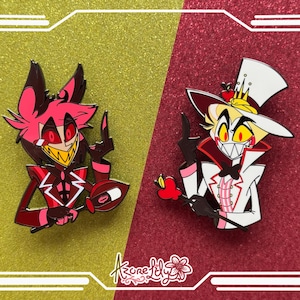 May include: Two enamel pins featuring cartoon characters. One pin has a red and black color scheme, with a yellow toothy grin. The other pin has a white and red color scheme, with a yellow toothy grin. Both pins are on a gold and red background.
