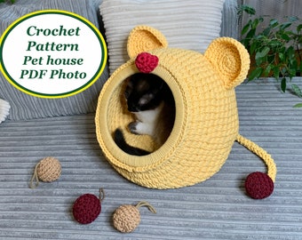 May include: A yellow crocheted pet house shaped like a lion with a cat inside. The house has a red nose and ears. There are three crocheted balls on the floor.
