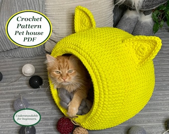 Könnte beinhalten: Ein hellgelbes Häkeltierhaus mit Katzenohren. Eine rotbraune Katze befindet sich im Haus. Der Text "Crochet Pattern Pet house PDF" befindet sich auf einem grünen Kreis. Der Text "Understandable for beginners." befindet sich auf einem grünen Oval.