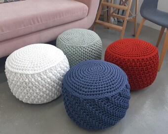 May include: Four crocheted footstools in different colors: white, light green, dark blue, and red. The footstools are round and have a textured surface.