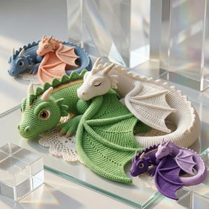 May include: A collection of handmade crochet dragons in various colors, including blue, peach, green, white, and purple. Each dragon features detailed wings and a sleeping expression. The dragons are displayed on a glass surface.
