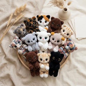 Könnte beinhalten: Eine Sammlung handgefertigter gehäkelter Katzenplüschtiere in verschiedenen Farben und Mustern, darunter Braun, Schwarz, Weiß und Schildpatt. Die Plüschtiere sind auf einem Holztablett angeordnet und zeigen ihre detaillierten Merkmale und weichen Texturen. Eine charmante und skurrile Präsentation.